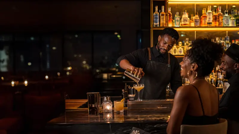 A bartender pours a cocktail at a lounge bar at night