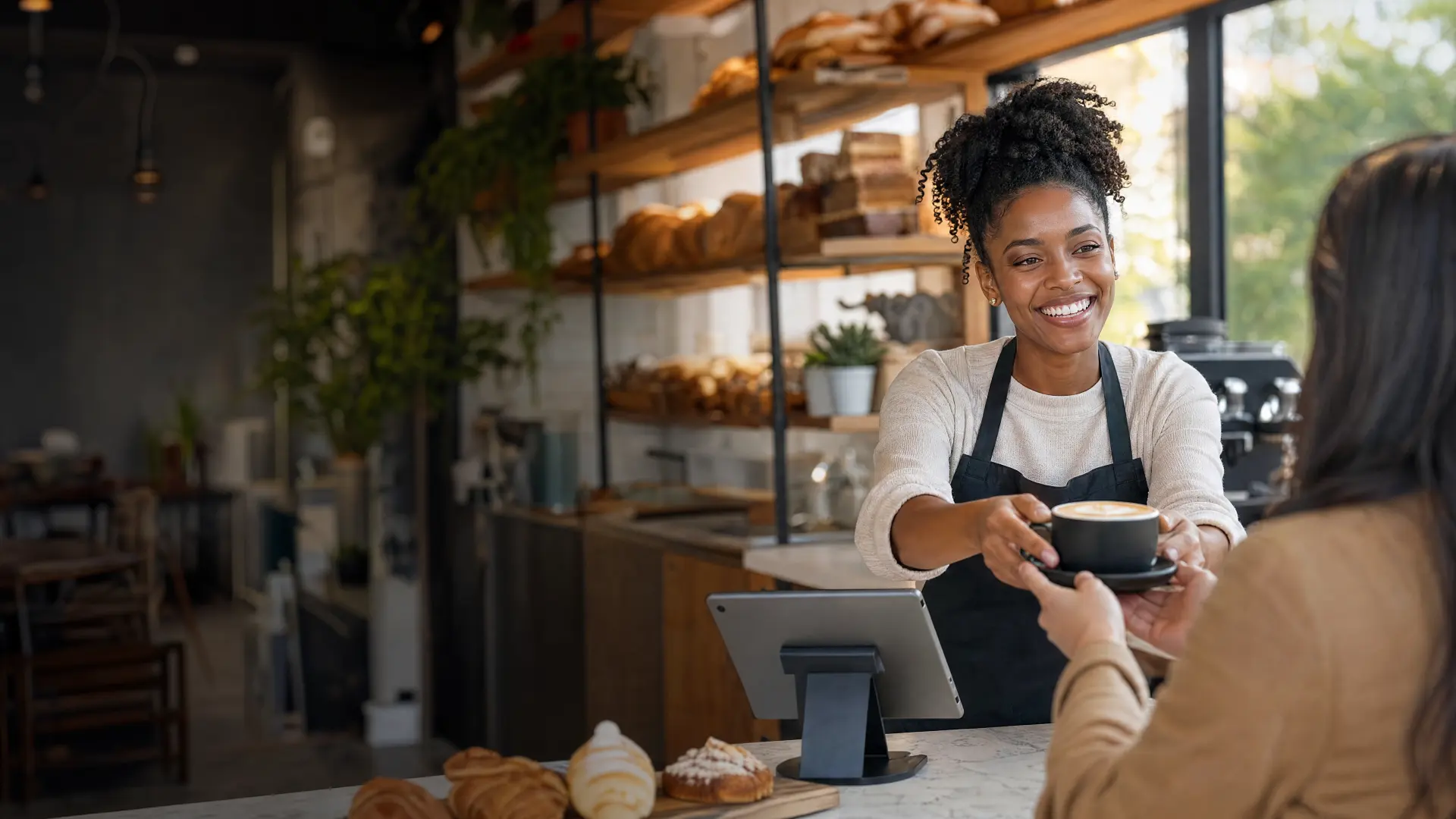 A barista hands a cappuccino across a bakery counter